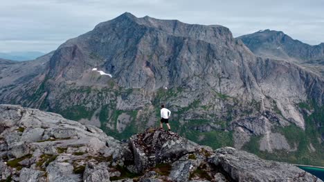 Hombre-De-Pie-Y-Admirando-La-Vista-Al-Borde-De-La-Montaña-Rocosa-De-Salberget-En-Flakstadvag,-Noruega