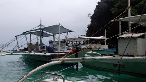 Traditional-Filipino-fishing-and-tour-outrigger-boats-moored-at-tourism-destination-during-island-hopping-tour-in-Palawan,-Philippines