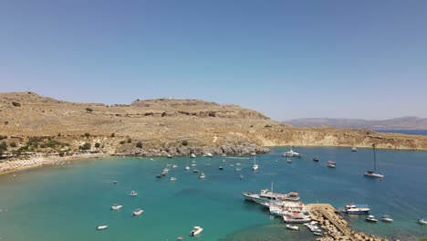 Lindos-beach,-famous-bay-in-Rhodes,-Greece-with-many-docked-boats,-aerial-dolly