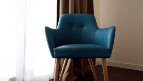 Langsam-Umlaufende-Aufnahme-Eines-Blauen-Stuhls,-Der-Neben-Dem-Fenster-In-Einem-Hotelzimmer-Sitzt