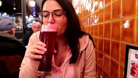 POV-shot-of-a-woman-sitting-in-a-pub-grabbing-a-large-pilsner-glass-of-red-beer