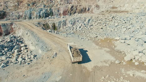 loaded-truck-driving-in-quarry-mineral-granite-stone-gravel-pit,-wide-aerial-drone-shot