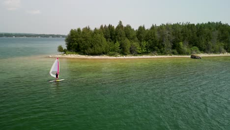 Aerial-view-of-windsurfer-going-along-shoreline,-Lake-Huron,-Michigan
