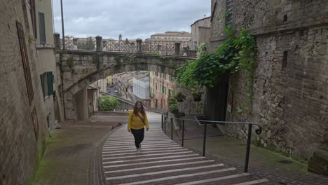 A-lone-female-walks-up-Via-Appia-below-the-historic-Via-dell'Acquedotto-in-Perugia,-Province-of-Perugia,-Italy