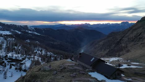 Drone-over-Bivacco-Marino-Bassi-mountain-cabin-with-epic-sunset-view-down-valley