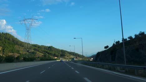 Driving-car-on-highway-through-beautiful-valley-with-hills-and-electricity-poles-on-a-summer-day-with-clear-blue-sky-in-Albania