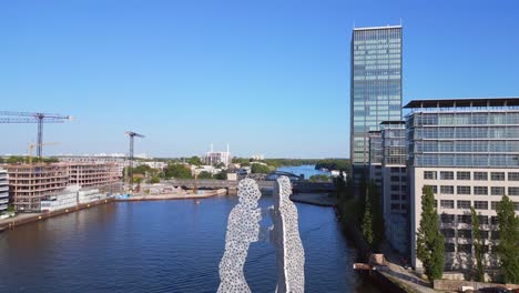 Skyscraper-Dramatic-aerial-top-view-flight-Molecule-Man-on-border-river-Spree,-east-Berlin-Germany-evening-summer-23