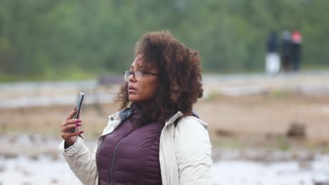mixed-race-woman-is-wearing-a-winter-travel-jacket-while-filming-with-her-smart-phone