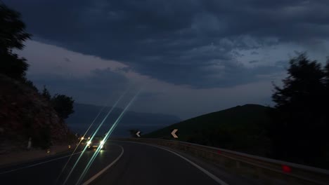 Mountain-road-over-Lin-village-in-Albania-at-twilight-with-dark-cloudy-sky,-traffic-driving-on-tourist-attraction-of-Ohrid-lake