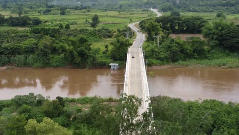Lone-vehicle-travels-over-bridge-with-river-below-and-onto-countryside-highway
