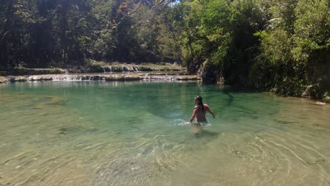 Latin-female-in-blue-bikini-walks-into-green-tropical-forest-river
