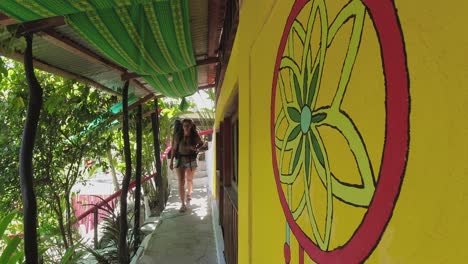 Young-Latin-female-backpacker-walks-along-bright-jungle-hostel-hallway
