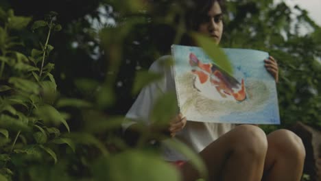 Slow-reveling-shot-of-a-young-teenager-holding-a-painting-of-fish-with-a-concept-of-conservation-of-the-ecosystem