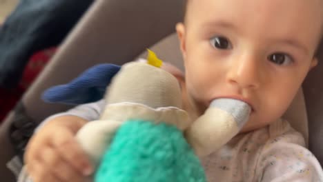 Cute-baby-with-a-toy-in-his-mouth,-rocking-his-chair-back-and-forth,-grabs-the-camera
