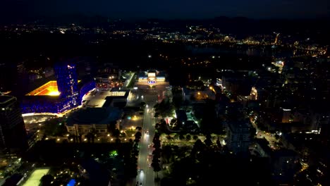 Zentraler-Boulevard-Der-Hauptstadt-Tirana-Bei-Nacht-Mit-Autos,-Die-Durch-Beleuchtete-Gebäude-Fahren,-Fantastische-Drohnenansicht-Der-Albanischen-Touristenattraktion