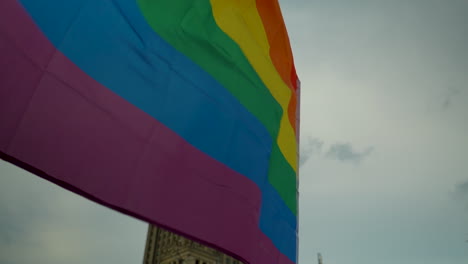 A-close-up-of-a-colorful-LGBT-flag-fluttering-against-the-backdrop-of-the-Palace-of-Culture-and-Science-in-Warsaw,-situated-on-the-main-square-in-the-heart-of-the-capital-city