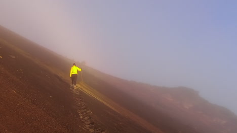Woman-in-yellow-jacket-climbs-foggy-volcanic-ash-slope-on-mountain
