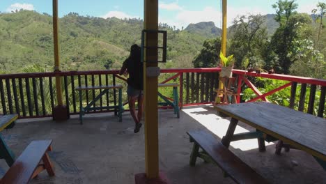 Latina-with-backpack-walks-to-balcony-rail-at-mountain-jungle-hostel