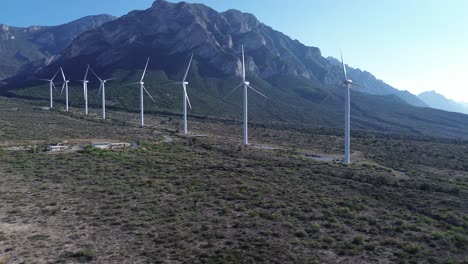 Große-Windkraftanlage,-Die-Am-Straßenrand-Steht,-Und-Dahinter-Sieht-Man-Einen-Großen-Berg-Und-Einen-Wirklich-Klaren-Himmel-Mit-Grünem-Gras-Auf-Dem-Boden