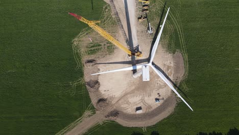 Crane-building-wind-turbine-in-green-fields,-top-down-view