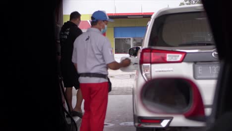 Gas-station-worker's-hand-holding-red-benzene-gas-pump,-filling-up-silver-mini-bus-car-tank-then-close-the-tank-again