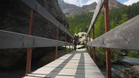 Wooden-Bridge-With-A-Man-Crossing-Over-Mountain-River-Stream-During-Hike