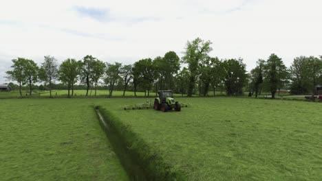 Tractor-driving-on-Dutch-grass-farmland,-drone-moving-around-subject