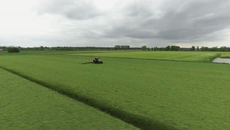 Tractor-Conduciendo-En-Tierras-De-Cultivo-De-Pasto-Holandés,-Drone-Moviéndose-Alrededor-Del-Sujeto