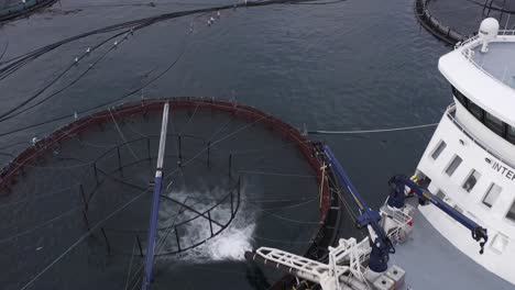 Reversing-drone-shot-of-a-well-boat-placing-fish-in-a-fish-farming-cage