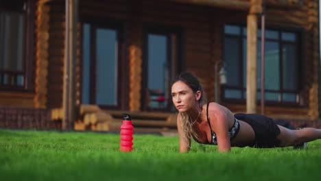 beautiful-brunette-on-the-background-of-a-large-mansion-engaged-in-fitness-and-performs-plank-exercise-for-the-press,-training-outdoors