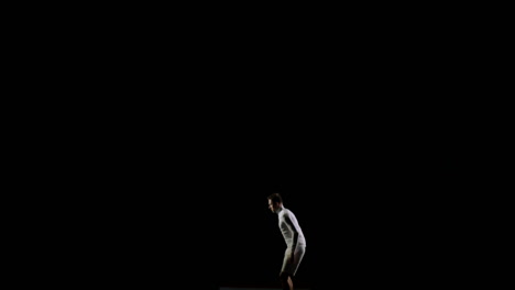 male-gymnast-on-a-black-background-in-white-clothes-soars-into-the-frame-from-below-and-makes-rotation-in-the-air-and-flips-in-slow-motion.-Gymnast-in-the-competition.-Individual-skill,-flight-and-concentration