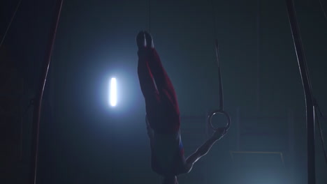 Gymnast-on-a-dark-background-stands-on-his-hands-using-rings-in-the-air.-Performs-rotation-in-the-Olympic-program