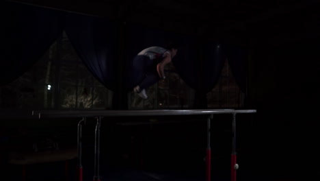 Male-gymnast-acrobat-performs-handstand-on-parallel-bars-in-a-dark-room-in-slow-motion