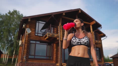 Curve-brunette-with-inflated-abdominal-muscles-drinking-protein-after-a-workout-against-the-backdrop-of-huge-houses-with-big-Windows