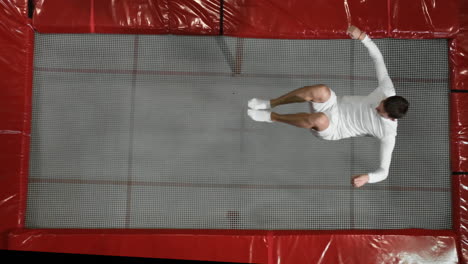 Top-view-gymnast-acrobat-in-white-clothes-performs-a-somersault-on-a-trampoline-in-slow-motion