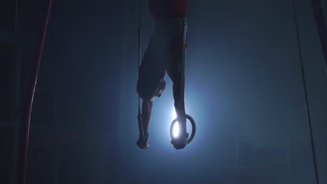 Gymnast-on-a-dark-background-stands-on-his-hands-using-rings-in-the-air.-Performs-rotation-in-the-Olympic-program-in-slow-motion-120-fps.-gymnastic-rings,-professional-gymnast