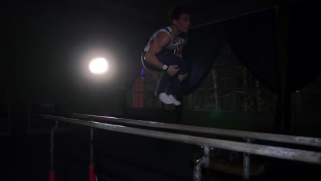 Male-gymnast-acrobat-performs-handstand-on-parallel-bars-in-a-dark-room-in-slow-motion-sharing-flips-and-landing-on-the-floor