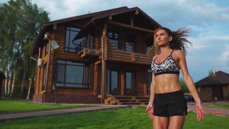 Slim-beautiful-woman-in-sportswear-on-the-background-of-the-house-on-the-lawn-performs-jumps-for-cardio-training-and-fat-burning