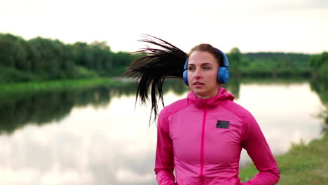 A-girl-in-a-pink-jacket-and-black-pants-runs-near-the-river-in-headphones-preparing-for-the-marathon