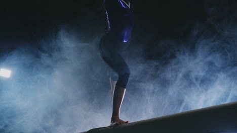 Close-up-of-the-leg-of-a-girl-gymnast-perform-a-balance-beam-jump-in-smoke-and-slow-motion.