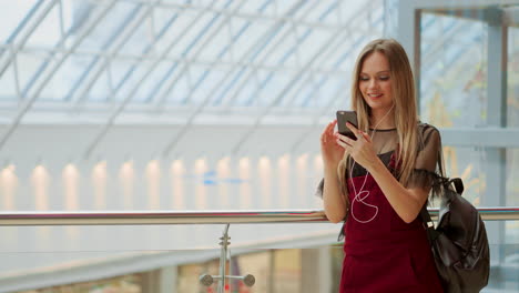 Happy-teenage-girl-holding-bags-with-purchases,-smiling-while-looking-at-phone-in-shopping-center.-Received-good-news,-reading-message,-texting.-Horizontal-photo-banner-for-website-header-design