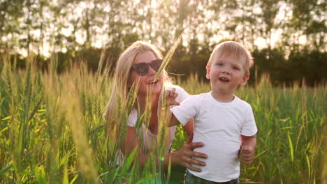 The-concept-of-a-happy-family.-In-the-rye-field,-the-kid-and-his-mother-are-fond-of-smiling-at-each-other-in-spikelets-in-the-backlight