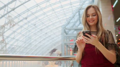 Happy-teenage-girl-holding-bags-with-purchases,-smiling-while-looking-at-phone-in-shopping-center.-Received-good-news,-reading-message,-texting.-Horizontal-photo-banner-for-website-header-design