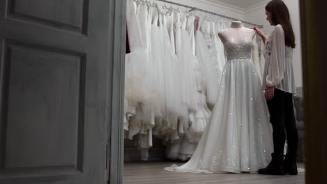 beautiful-girl-looking-wedding-dress-in-the-cabin-compared-to-other-dresses.-Preparing-for-the-wedding.-Buying-a-wedding-dress.-The-seamstress-inspects-the-finished-custom-made-wedding-dress.