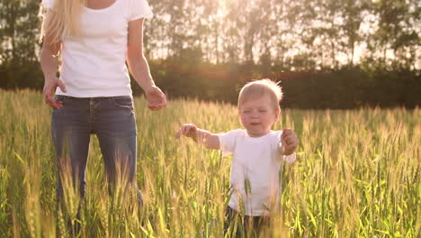 The-concept-of-a-happy-family.-In-the-rye-field,-the-kid-and-his-mother-are-fond-of-smiling-at-each-other-in-spikelets-in-the-backlight