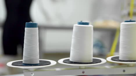 Closeup-of-three-big-bobbins-with-thin-white-thread-on-working-professional-sewing-machine.-Real-time-full-hd-video-footage