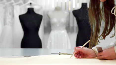 Eine-Schöne-Modedesignerin-Greift-Auf-Papiervorlagen-Zurück,-Um-Stoff-Für-Schaufensterpuppen-In-Hochzeitskleidern-Auszuschneiden.-Hersteller-Von-Brautkleidern.