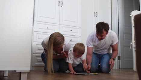 A-family-of-three-in-white-T-shirts-and-blue-jeans-sitting-on-the-floor-of-their-bedroom-playing-with-the-boy-in-intellectual-games.-Slow-motion-shooting-happy-family