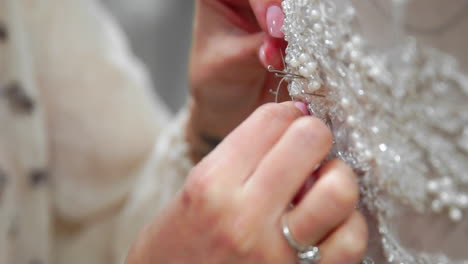 Close-up-fashion-designer-for-brides-in-his-Studio-pins-needles-lace-wedding-dress.-Seamstress-creates-an-exclusive-wedding-dress.-Secure-with-pins-and-needles-outline.-Small-private-business.-Sew-rhinestones-and-crystals-to-the-dress-thread-and-needle.-Jewelry-work.