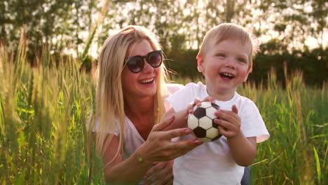 The-concept-of-a-happy-family.-Close-up-of-a-boy-and-his-mother-in-a-field-with-wheat-spikes-smiling-and-playing-with-a-soccer-ball